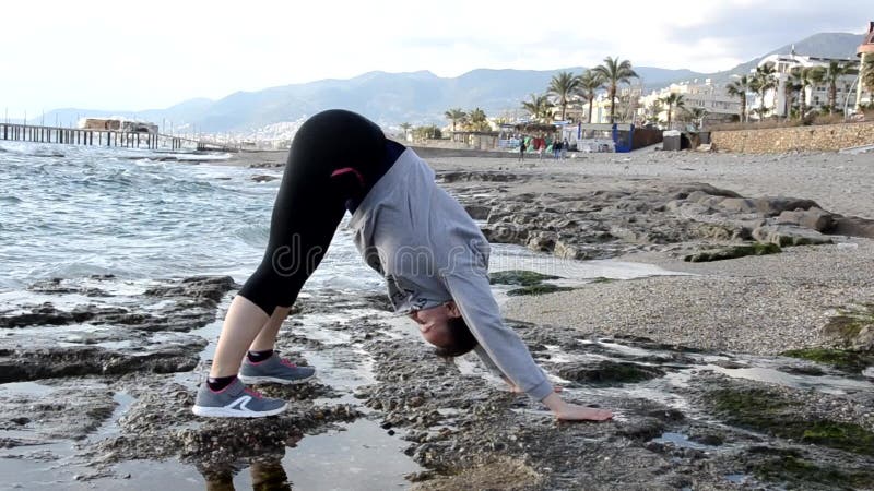 Prachtige blond meisjeskleding in de zee aan de rots waar yoga zich uitstrekt tot stromende of sportgymnastiek en