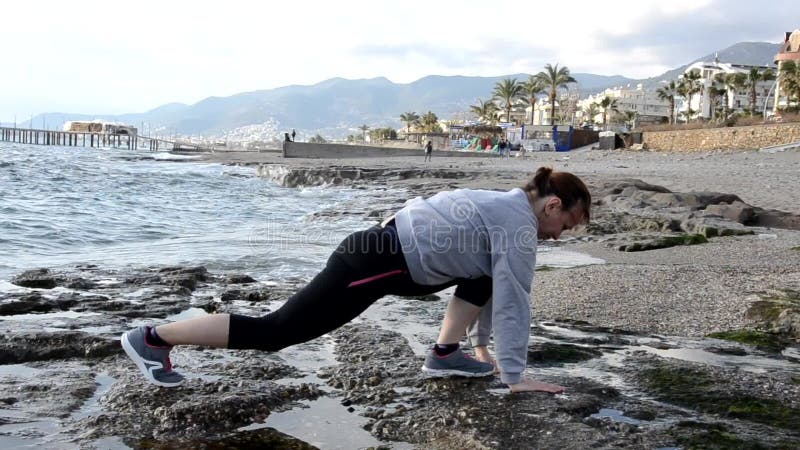 Prachtige blond meisjeskleding in de zee aan de rots waar yoga zich uitstrekt tot stromende of sportgymnastiek en