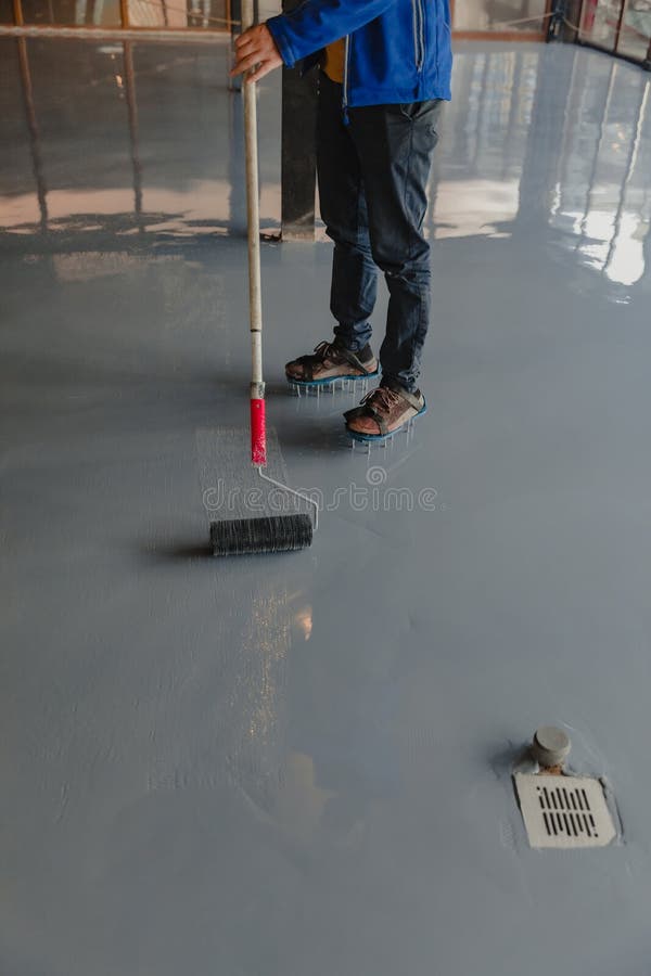 The worker applies gray epoxy resin to the new floor. The worker applies gray epoxy resin to the new floor