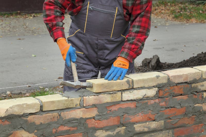 Mason making wall with mortar and bricks, using hammer tool. Mason making wall with mortar and bricks, using hammer tool