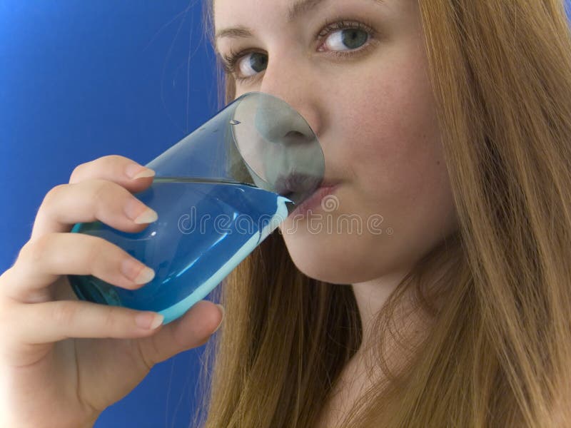 Woman drinking water out of a colored glass, staring into the camera. Woman drinking water out of a colored glass, staring into the camera.