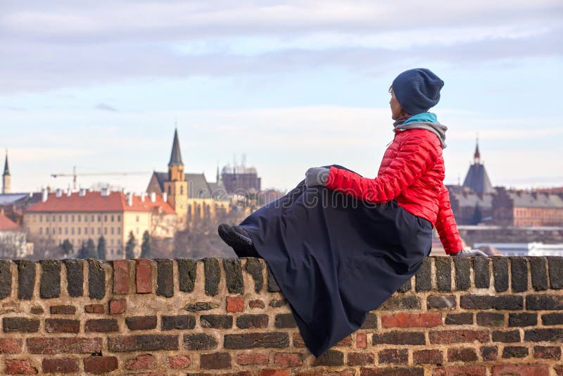 Prague. A young woman in a red jacket sits on a brick wall and admires the view of the historical part of the city of Prague, Czec stock photography Prague. A young woman in a red jacket sits on a brick wall and admires the view of the historical part of the city of Prague, Czec stock photography
