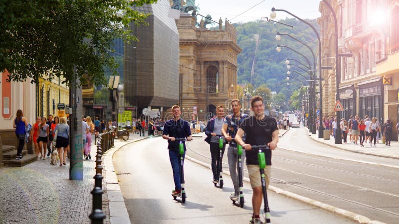 Cheerful young people move on electric scooters along the street in the center of Prague