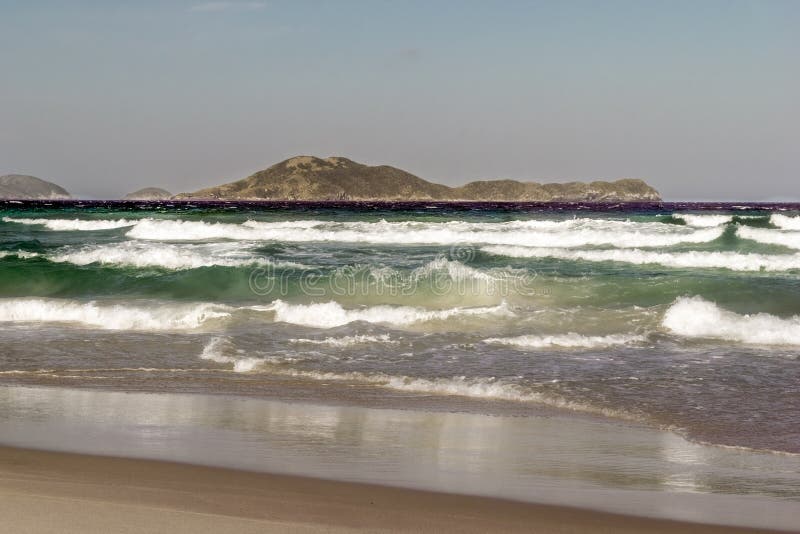 Praia das dunas με κύματα ωκεανού που καλύπτουν τον γαλάζιο ουρανό της παραλίας και τα βουνά στο φόντο. στοκ εικόνες