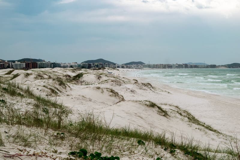 Praia das dunas με μια όμορφη θαλάσσια λευκή αμμώδη θόλο και την πόλη στο παρασκήνιο. στοκ φωτογραφία