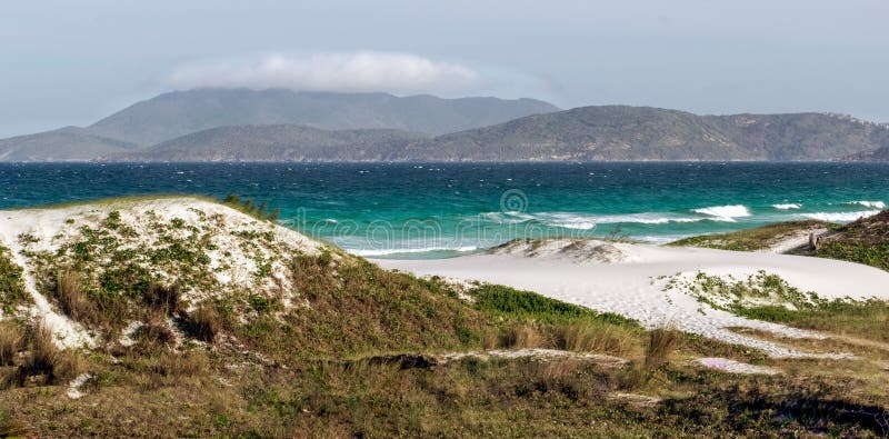Praia das dunas με υπανάπτυξη από τον γαλάζιο ουρανό και τα βουνά στο φόντο. στοκ εικόνα