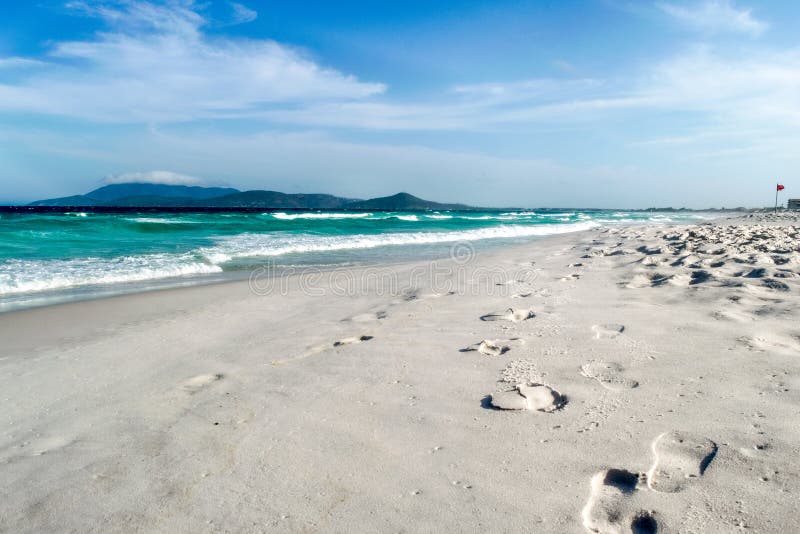 Praia das dunas με όμορφα θαλάσσια αποτυπώματα στη λευκή άμμο και το βουνό στο φόντο. στοκ φωτογραφίες