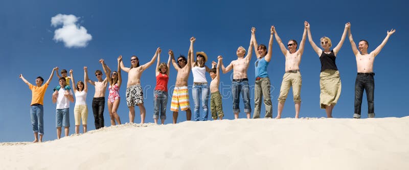 Image of many friends standing on sandy beach with their arms raised against blue sky. Image of many friends standing on sandy beach with their arms raised against blue sky