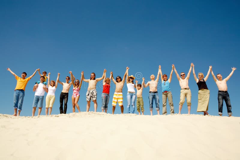 Image of many friends standing on sandy beach with their arms raised against blue sky. Image of many friends standing on sandy beach with their arms raised against blue sky