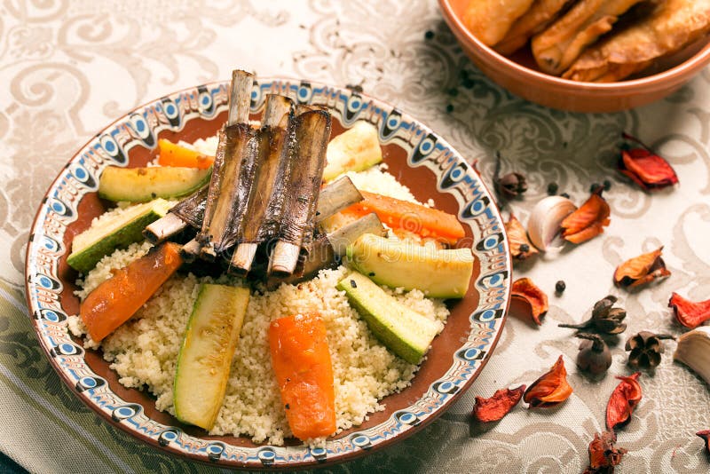 Traditional couscous dish with lamb ribs and vegetables. Still life with rose petals on the table. The image is describing moroccan culture. Traditional couscous dish with lamb ribs and vegetables. Still life with rose petals on the table. The image is describing moroccan culture