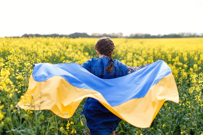 Child with Ukrainian flag in rapeseed field. A girl in an embroidered shirt runs across the field with the Ukrainian flag in her