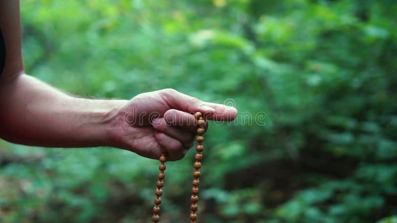 Prayer beads in hand. Male hand holding rosary, praying to god on green nature background, religious spirituality.