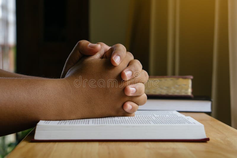 Prayer hands on a Holy Bible on wood table with window light.christian backgound.closeup concept.