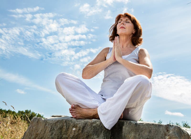 Praying beautiful middle aged woman in yoga position over blue sky