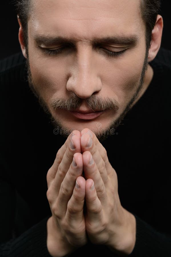 Praying with eyes closed. Devout bearded man praying and holding