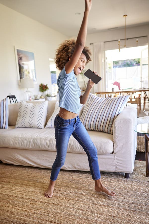 Pre-tiener Afrikaans Amerikaans meisje die en in de woonkamer dansen zingen die thuis haar telefoon met behulp van als microfoon, stock foto's Pre-tiener Afrikaans Amerikaans meisje die en in de woonkamer dansen zingen die thuis haar telefoon met behulp van als microfoon, stock foto's