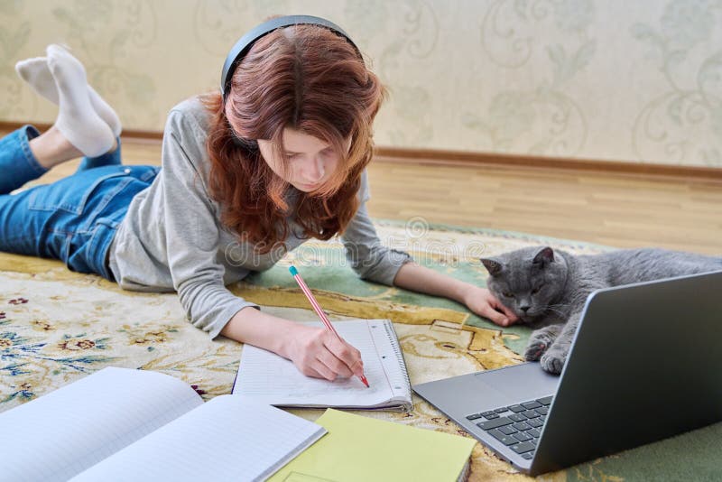 Preadolescente estudiando en auriculares con laptop tendida en el suelo con gato foto de archivo