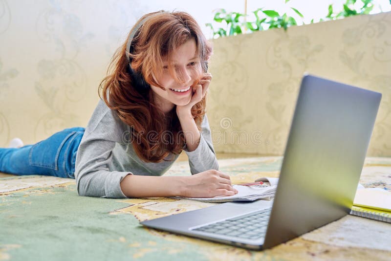 Preadolescente estudiando en auriculares con portátil en el suelo en casa fotografía de archivo