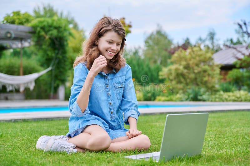 Preadolescente sentada en césped de patio trasero usando laptop para el ocio y el estudio imagen de archivo