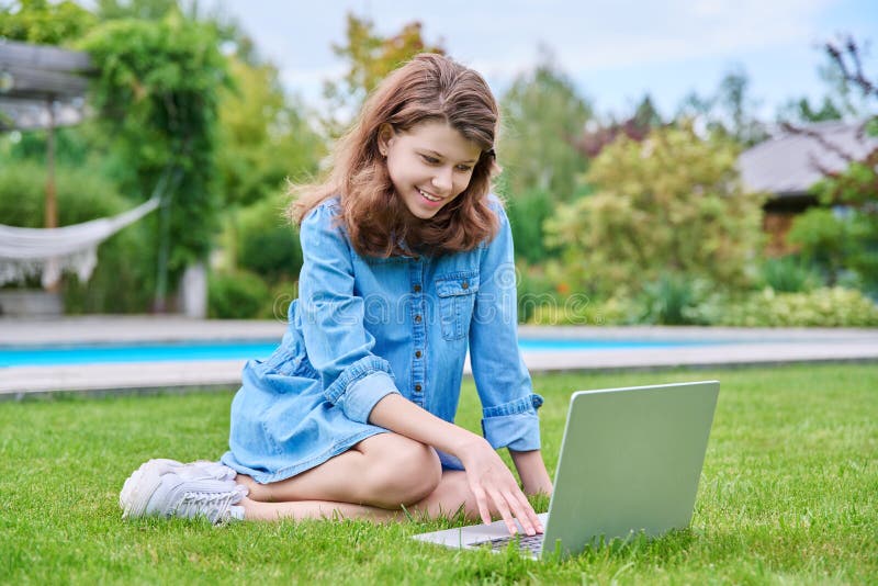 Preadolescente sentada en césped de patio trasero usando laptop para el ocio y el estudio imagen de archivo
