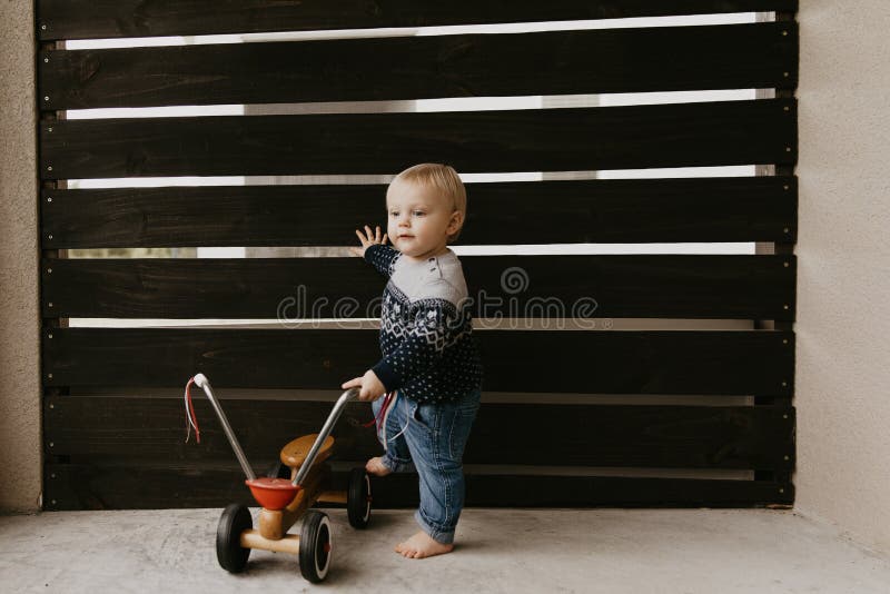 Precious Adorable Cute Little Blonde Baby Toddler Boy Kid Playing Outside on Wooden Toy Bicycle Scooter Mobile Smiling at the Camera and Having Fun at home on back patio