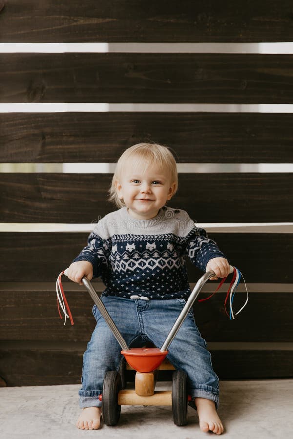 Precious Adorable Cute Little Blonde Baby Toddler Boy Kid Playing Outside on Wooden Toy Bicycle Scooter Mobile Smiling at the Camera and Having Fun at home on back patio