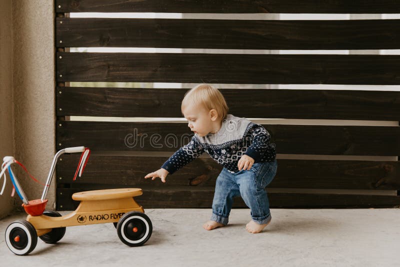 Precious Adorable Cute Little Blonde Baby Toddler Boy Kid Playing Outside on Wooden Toy Bicycle Scooter Mobile Smiling at the Camera and Having Fun at home on back patio