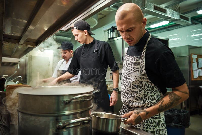 Precise mais especiarias Cozinheiro chefe profissional sério com diversas tatuagens em sua terra arrendada de braços uma bandeja fotos de stock royalty free Precise mais especiarias Cozinheiro chefe profissional sério com diversas tatuagens em sua terra arrendada de braços uma bandeja fotos de stock royalty free
