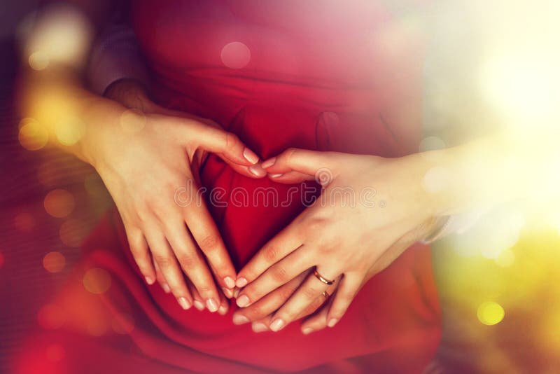 Pregnancy and family love concept. Expecting parents holding heart shape hands