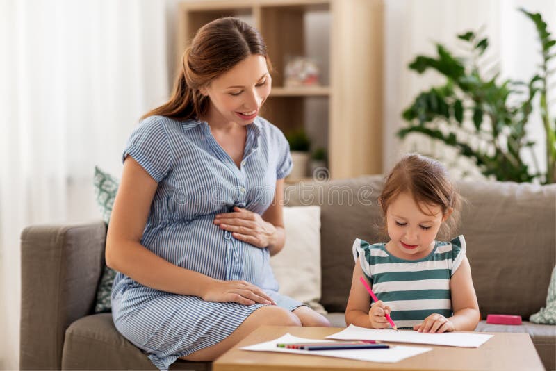 Pregnancy, people and family concept - happy pregnant mother and little daughter drawing at home. Pregnancy, people and family concept - happy pregnant mother and little daughter drawing at home