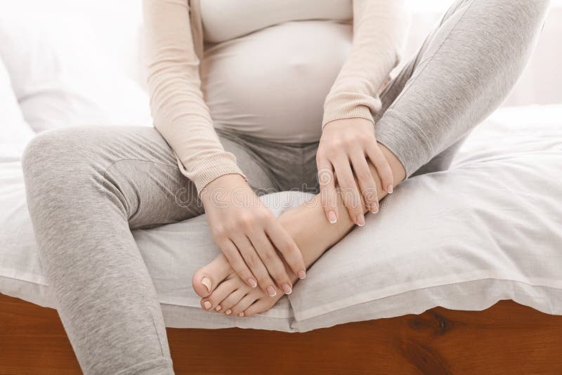Pregnant woman massaging her swollen foot sitting on bed