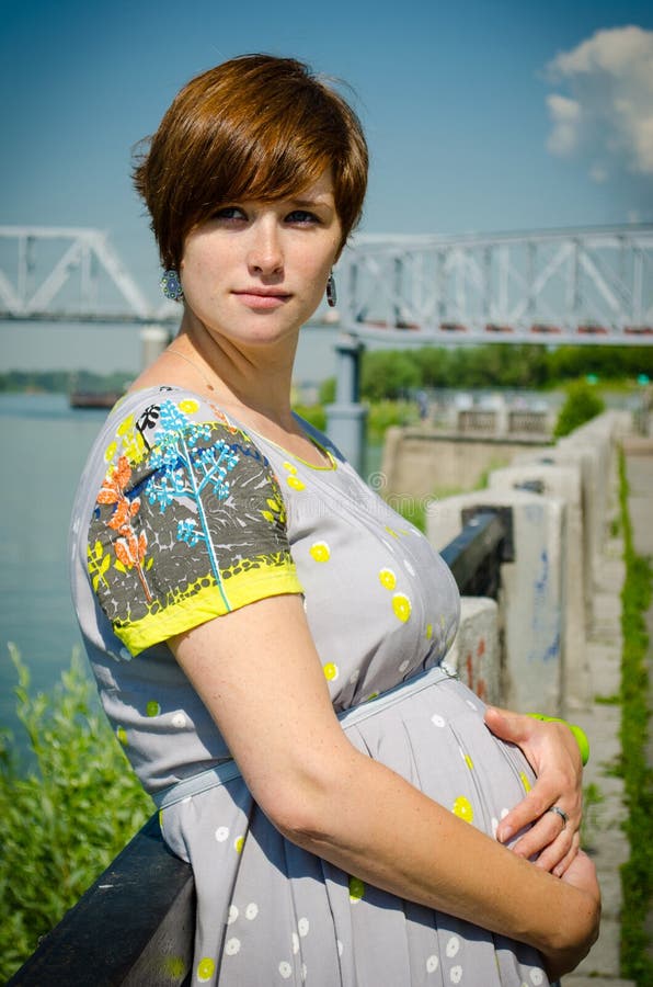 Pregnant beautiful young woman by embankment, near the river