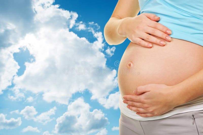 Pregnant belly over blue cloudy sky