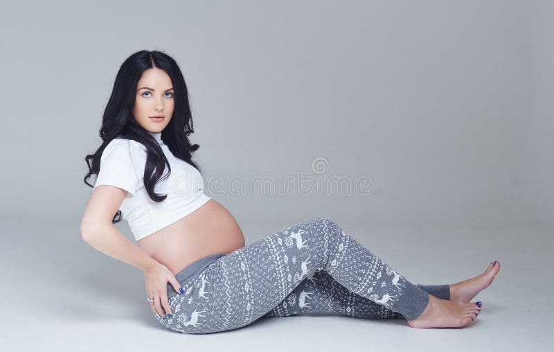 Pregnant brunette woman sits on a floor.