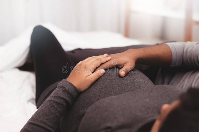 Pregnant couple with hands on belly lying on bed royalty free stock images