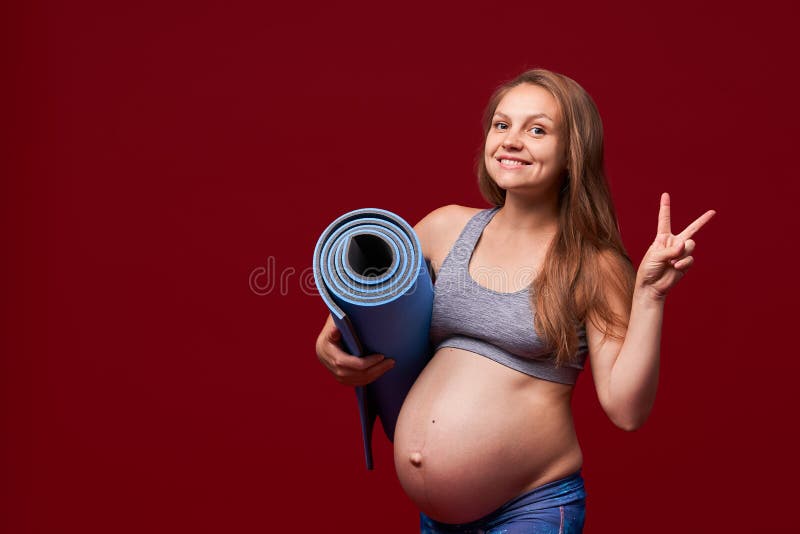 Pregnant girl holding a sports Mat in her hands, shows a gesture of victory. positive smiling woman in sports clothes pregnant royalty free stock image Pregnant girl holding a sports Mat in her hands, shows a gesture of victory. positive smiling woman in sports clothes pregnant royalty free stock image