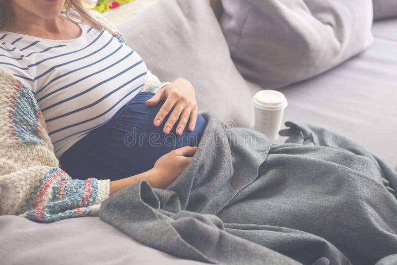 Pregnant happy woman sitting and drinking hot coffee or tea in the cafe on the terrace, covering his legs with a rug