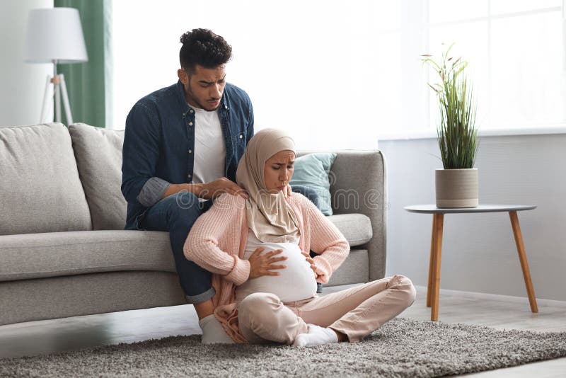 Pregnant muslim lady suffering prenatal contractions at home, caring husband comforting her