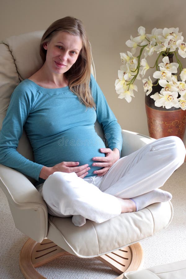 Tehotná žena v modrom drese sedí pohodlne na pohovka kreslo.