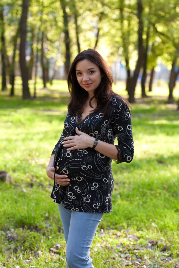 Pregnant woman in blue jeans walking in park