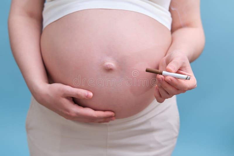 Pregnant woman with a cigarette in her hand, blue background in the studio.