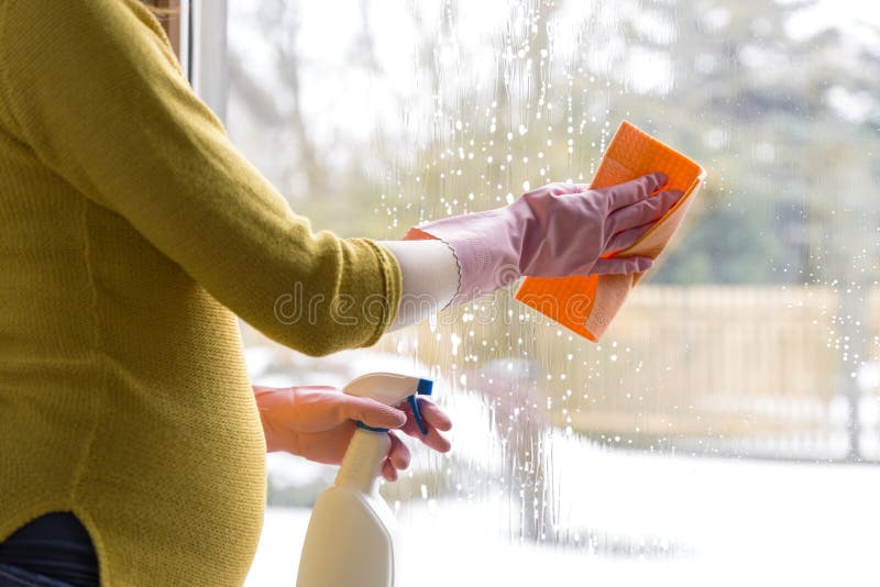 Pregnant woman cleaning window with cloth and window spray. Sping cleaning concept