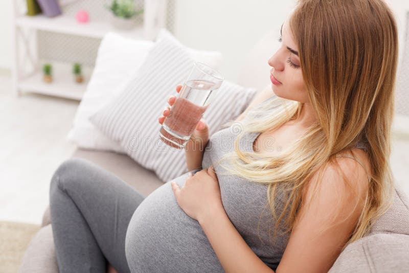 Pregnant woman with glass of water sitting on sofa closeup royalty free stock photography Pregnant woman with glass of water sitting on sofa closeup royalty free stock photography