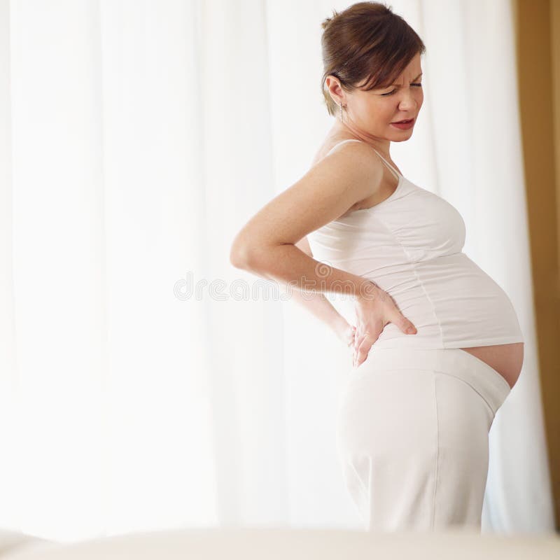 Asian pregnant woman in black undershirt sitting on white bed and