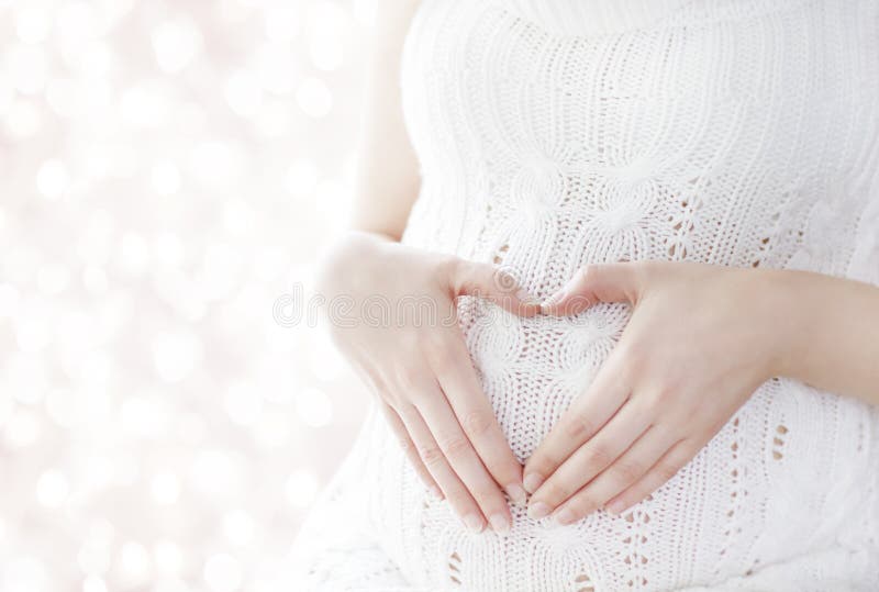 Pregnant Woman Heart Shape, Pregnancy Concept, Maternity Belly. Care, White Woolen Dress, unfocused bokeh background royalty free stock images Pregnant Woman Heart Shape, Pregnancy Concept, Maternity Belly. Care, White Woolen Dress, unfocused bokeh background royalty free stock images