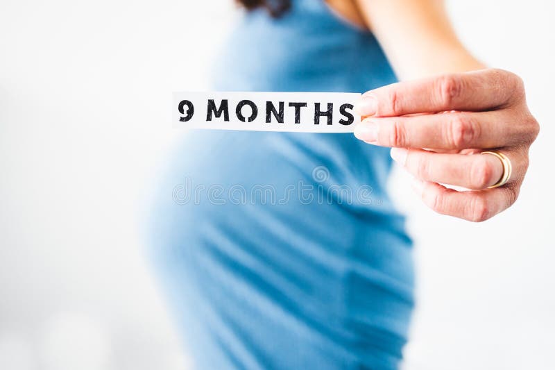 Pregnant woman holding 9 Months sign towards the camera wearing blue dress in the last month of pregnancy stock photography Pregnant woman holding 9 Months sign towards the camera wearing blue dress in the last month of pregnancy stock photography