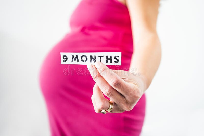 Pregnant woman holding 9 Months sign towards the camera wearing pink dress in the last month of pregnancy stock images Pregnant woman holding 9 Months sign towards the camera wearing pink dress in the last month of pregnancy stock images