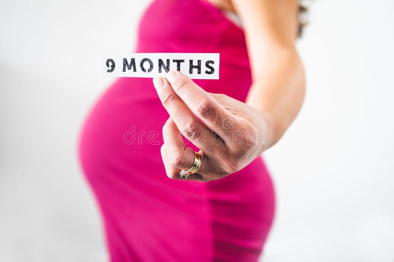 Pregnant woman holding 9 Months sign towards the camera wearing pink dress in the last month of pregnancy stock photography Pregnant woman holding 9 Months sign towards the camera wearing pink dress in the last month of pregnancy stock photography