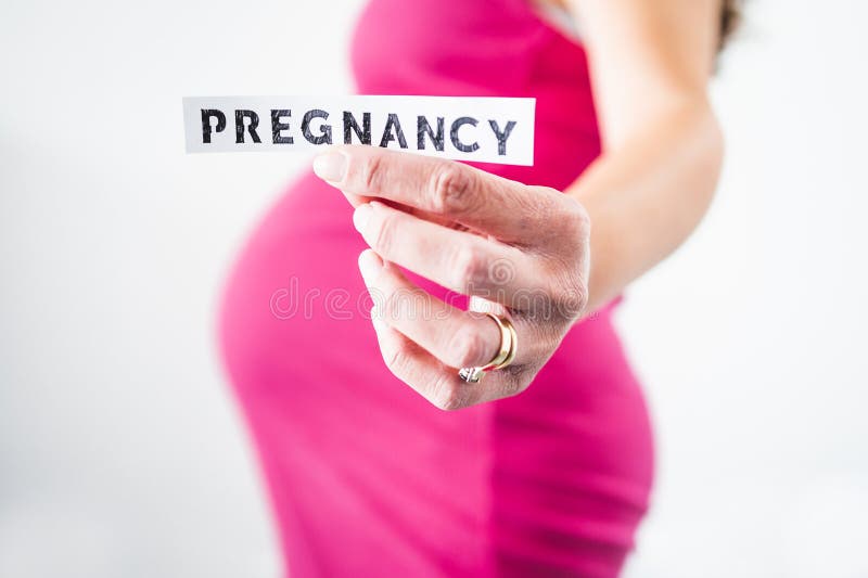 Pregnant woman holding Pregnancy sign towards the camera wearing pink dress in the last month of pregnancy stock photo Pregnant woman holding Pregnancy sign towards the camera wearing pink dress in the last month of pregnancy stock photo