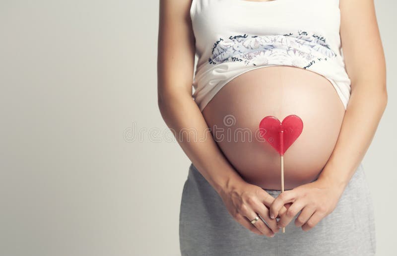 Pregnant woman holds red heart candy.